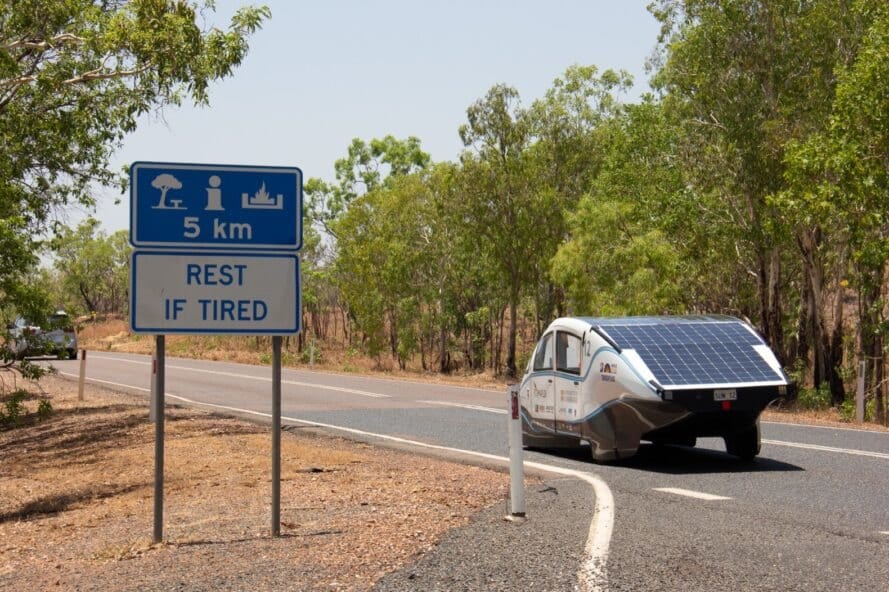white car with solar panels driving on a road