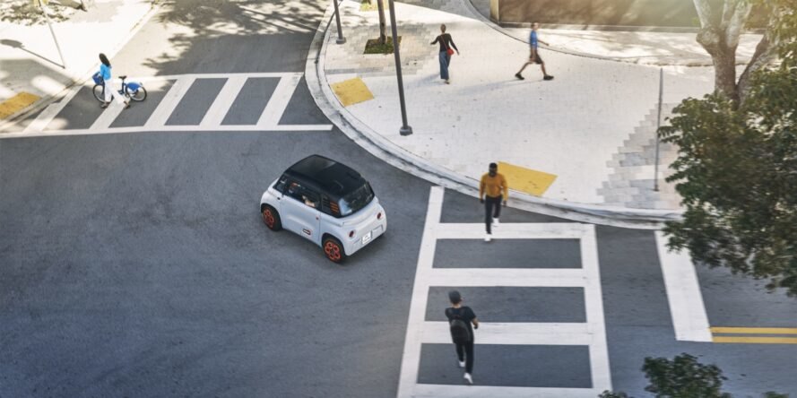 tiny gray electric car waiting as people cross at a crosswalk